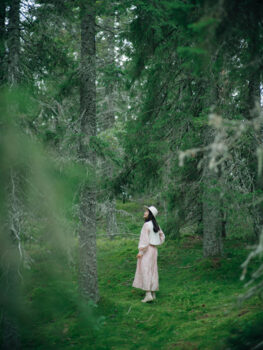 A woman in a pink dress walks in a green forest.