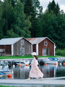 A woman is walking on a jetty. In the background are boats and wooden houses.