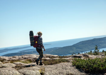 A woman with a backpack is hiking on one of the peaks of the Swedish High Coast overlooking the Baltic Sea.